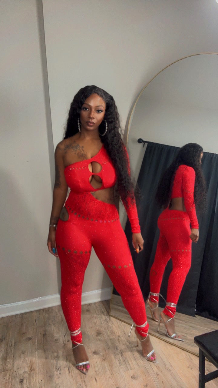 She models a bright red one-piece lace jumpsuit with silver rhinestone embellishments.