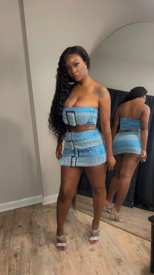 She is modeling a light blue denim bedazzled  two-piece set consisting of a strapless crop top and a matching mini skirt. 